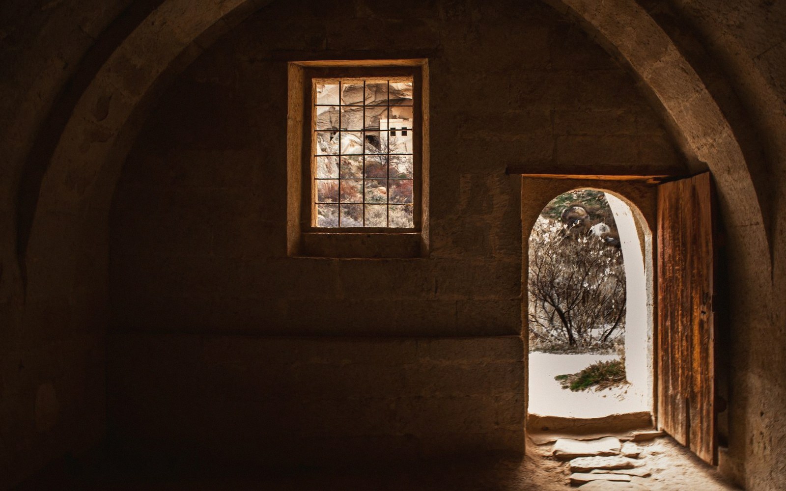 Open wooden door and barred window in a stone chamber with vaulted ceiling