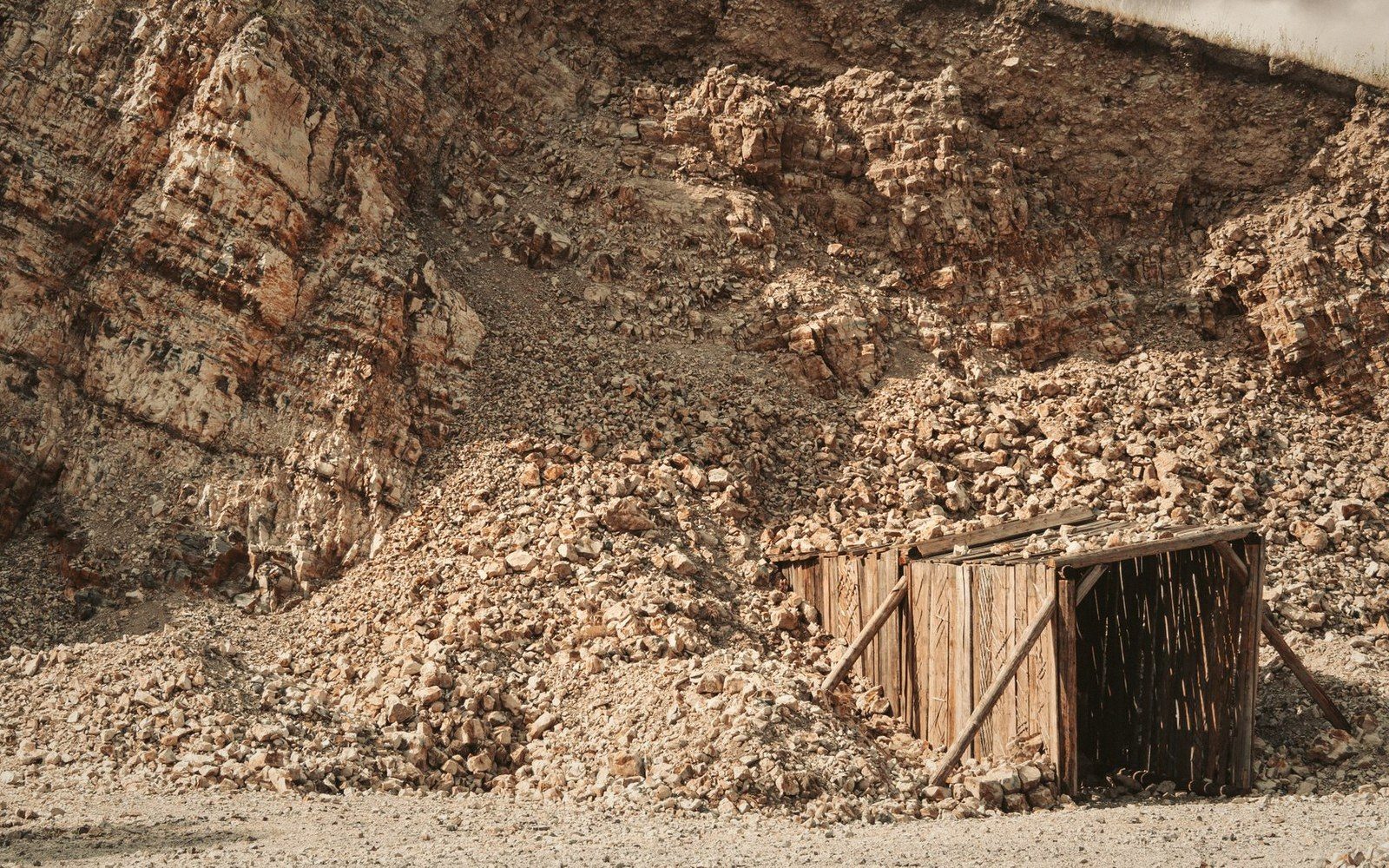 A collapsed rock quarry face with rubble piling against a wooden mine entrance structure