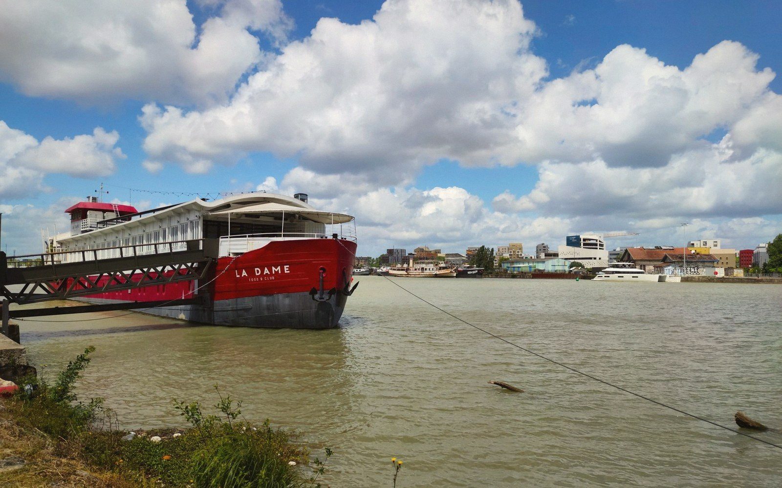 The red boat "La Dame" moored on a wide river beside a distant city skyline