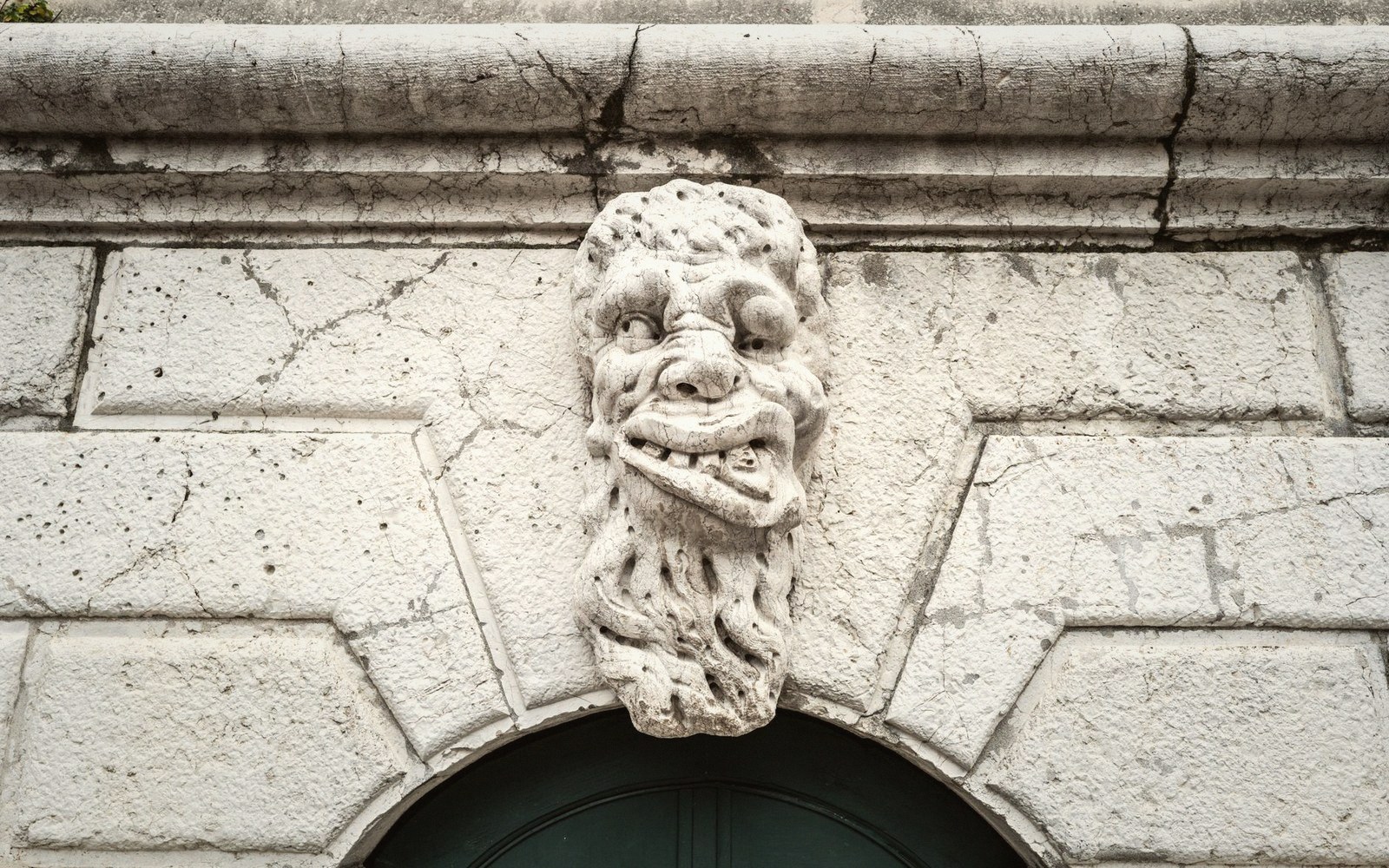 Grimacing carved stone face mounted above an arched doorway on a weathered wall